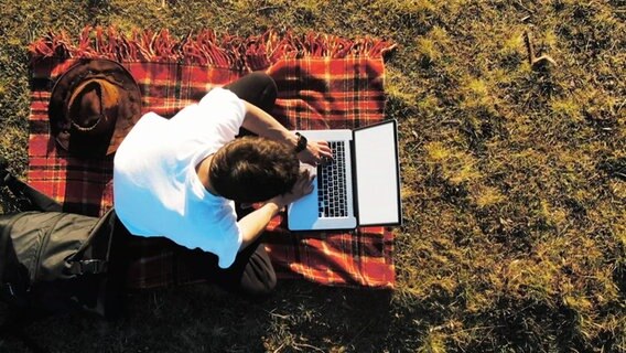 Eine Person sitzt an einem Laptop auf einer Decke im Freien. © Screenshot 