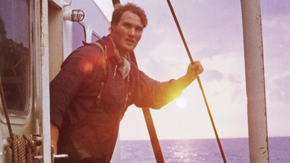 Ein junger Mann auf einem Schiff mit der Sonne hinter sich.  
