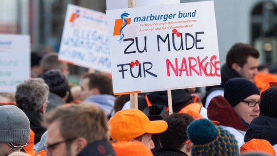 Ärzte stehen bei einem Warnstreik vor dem Hannover Hauptbahnhof und halten ein Schild mit der Aufschrift "Zu müde für Narkose" hoch. © dpa-Bildfunk Foto: Julian Stratenschulte